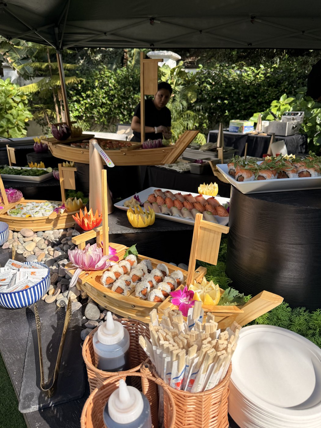 A SŌKAI sushi station under a tent — bamboo boats, orchids, ginger and wasabi bowls set for service